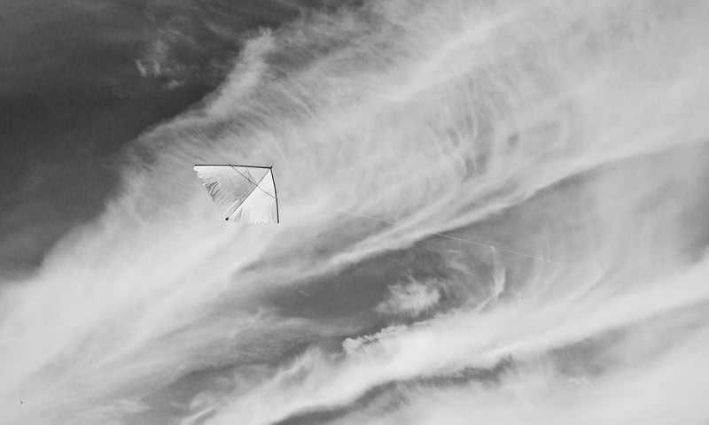A white kite floating in front of clouds.