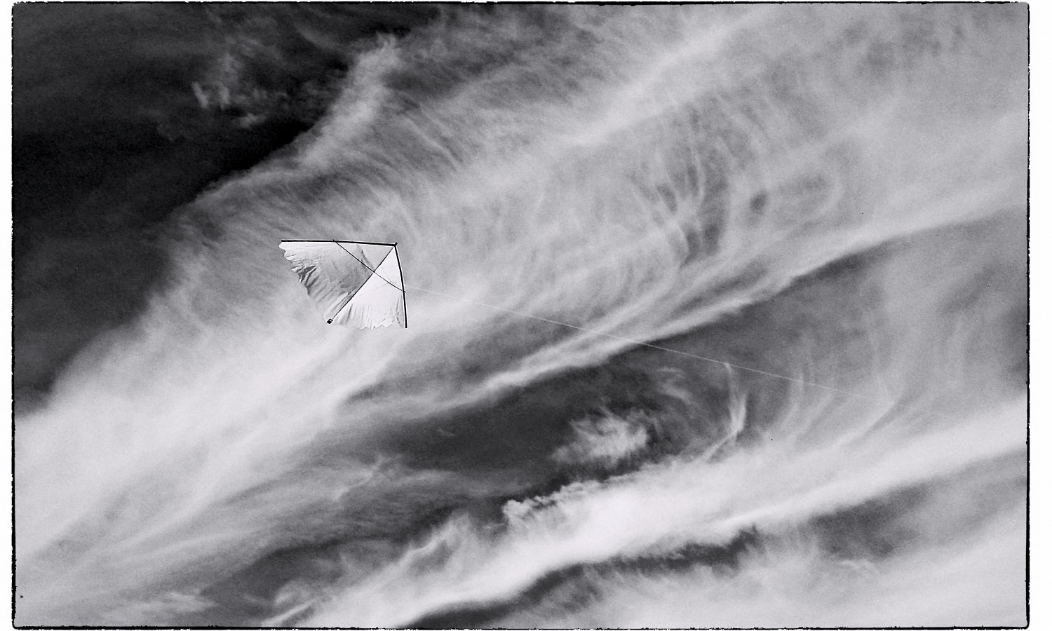 A white kite floating in front of clouds.